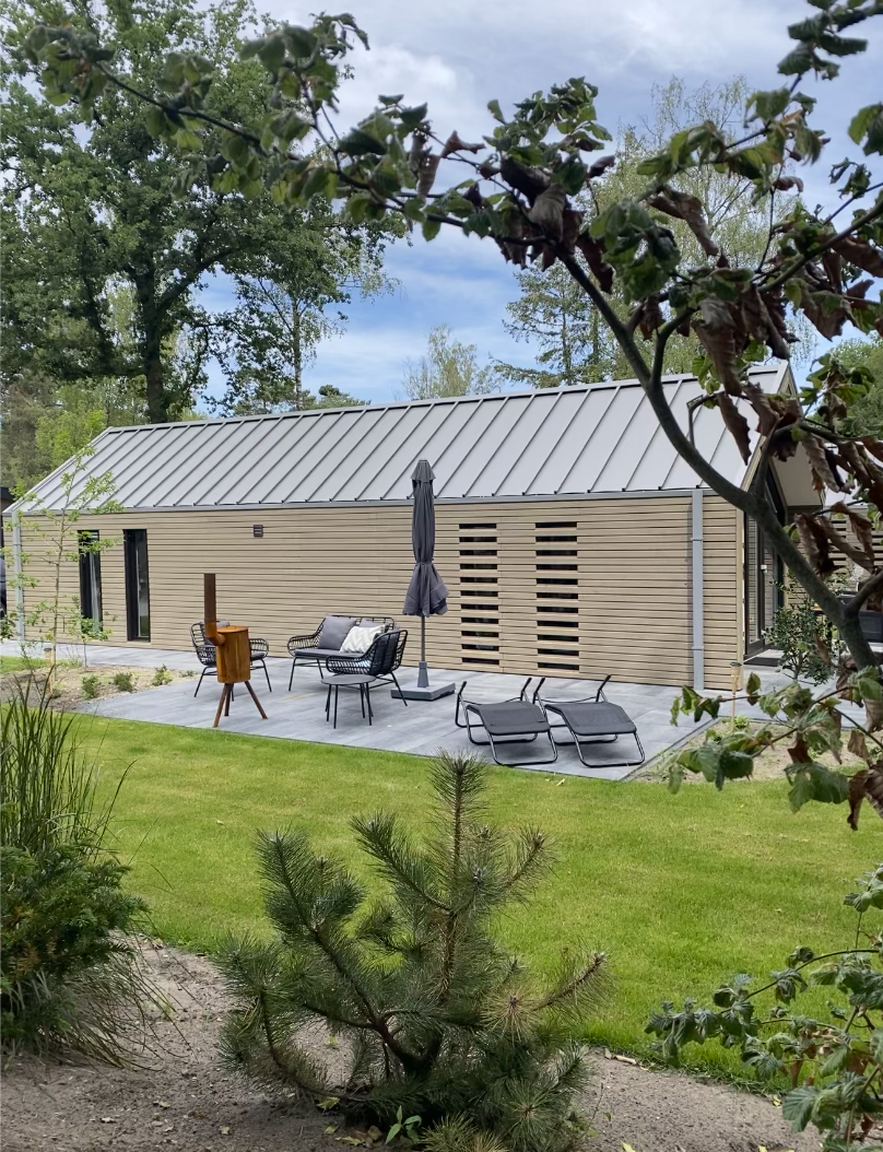 Houten natuurhuisje met een terras en ligstoelen tussen de bomen.