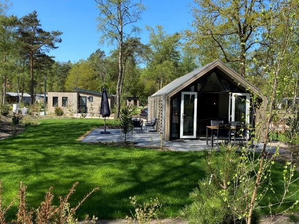 Voorzijde van het natuurhuisje met open tuindeuren, een terras en een groene tuin.